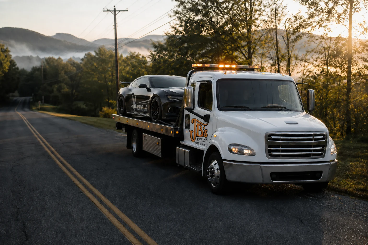A JB's Towing rollback carrying a black Camaro on an East Tennessee road